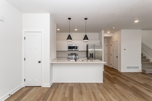 kitchen with appliances with stainless steel finishes, hanging light fixtures, a textured ceiling, white cabinets, and tasteful backsplash