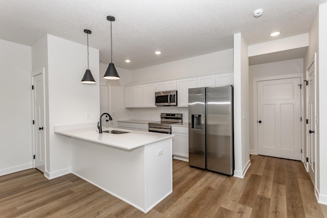 kitchen with stainless steel appliances, hanging light fixtures, kitchen peninsula, sink, and white cabinetry