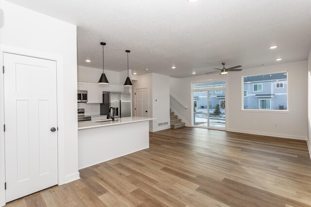 kitchen with stainless steel appliances, white cabinetry, ceiling fan, light hardwood / wood-style floors, and hanging light fixtures