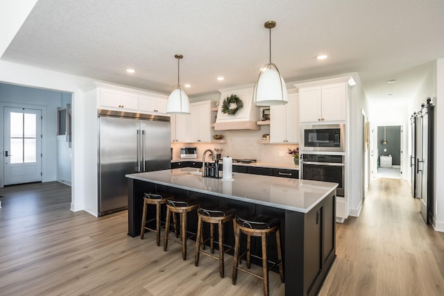 kitchen featuring built in appliances, a kitchen island with sink, white cabinets, and a barn door