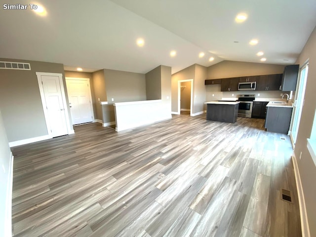 kitchen with sink, light hardwood / wood-style floors, lofted ceiling, a kitchen island, and appliances with stainless steel finishes