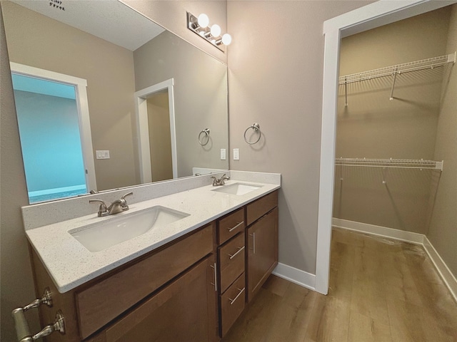 bathroom featuring double vanity, baseboards, a sink, and wood finished floors