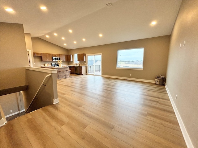 1677 20th Ave SE, Altoona, IA 50009 - kitchen featuring light countertops, stainless steel microwave, light wood finished floors, lofted ceiling, and open floor plan