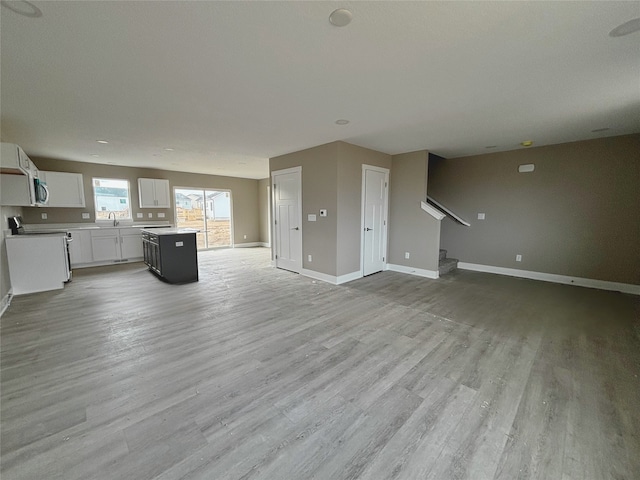 unfurnished living room with light wood-type flooring, stairs, baseboards, and a sink