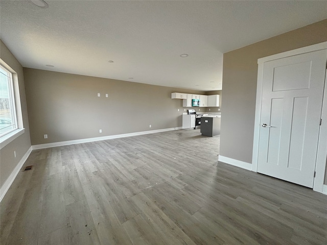 unfurnished living room featuring visible vents, baseboards, and wood finished floors