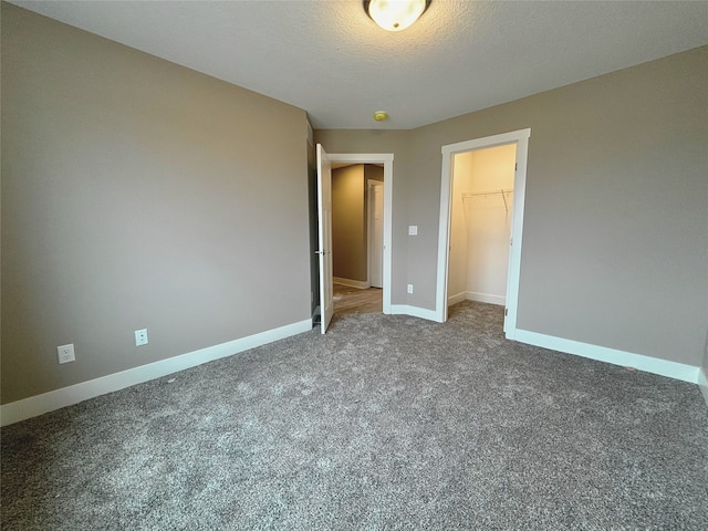 unfurnished bedroom with carpet floors, a closet, a spacious closet, a textured ceiling, and baseboards