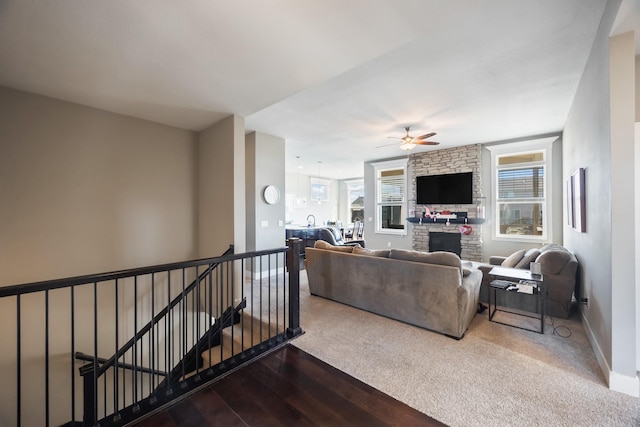 living room featuring ceiling fan, a stone fireplace, and wood-type flooring