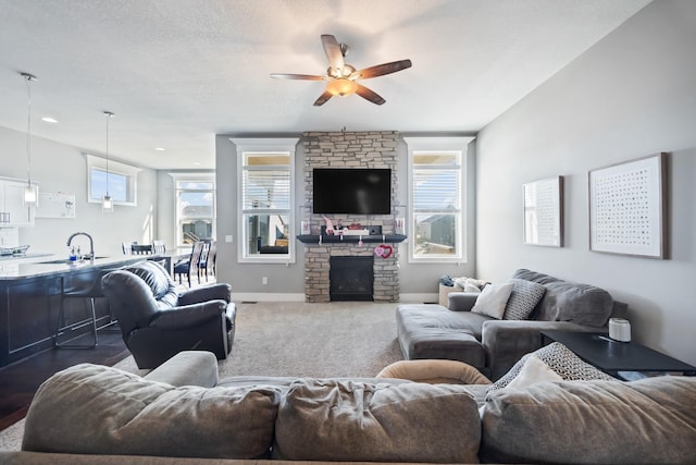 living room featuring a stone fireplace, ceiling fan, sink, and a textured ceiling