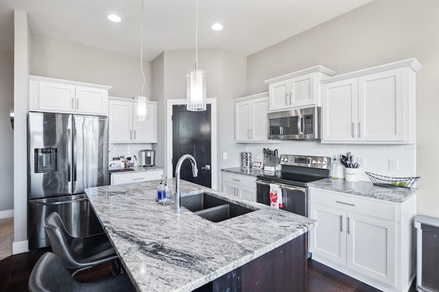 kitchen featuring white cabinetry, sink, stainless steel appliances, decorative light fixtures, and a kitchen island with sink