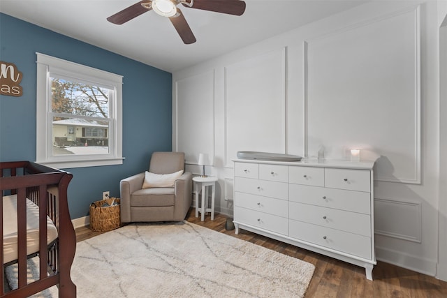 bedroom featuring a nursery area, dark wood-type flooring, and ceiling fan