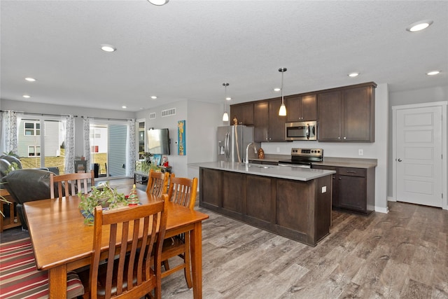 kitchen with a center island with sink, sink, decorative light fixtures, dark brown cabinets, and stainless steel appliances