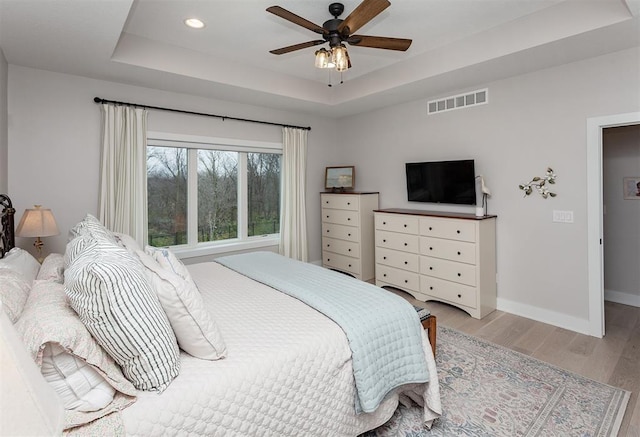 bedroom featuring light hardwood / wood-style flooring, a raised ceiling, and ceiling fan