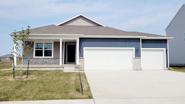 view of front of house featuring a front yard, stone siding, an attached garage, and concrete driveway