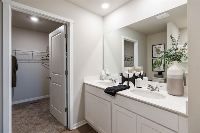 bathroom featuring a sink, a walk in closet, baseboards, and double vanity