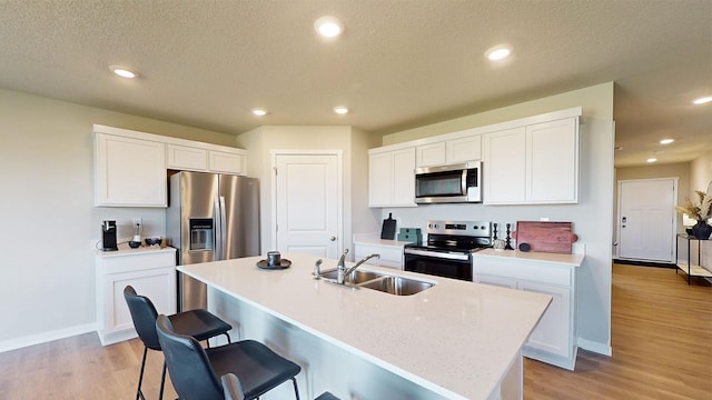 kitchen with sink, a kitchen island with sink, white cabinetry, stainless steel appliances, and light hardwood / wood-style floors