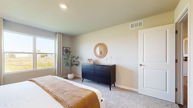 bedroom featuring baseboards, a textured ceiling, visible vents, and light colored carpet