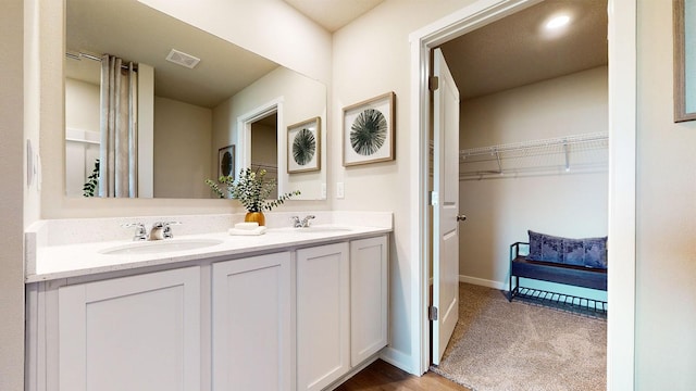 full bath with double vanity, a spacious closet, visible vents, and a sink