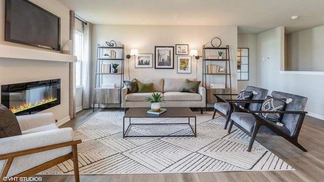 living room featuring a glass covered fireplace, baseboards, and wood finished floors