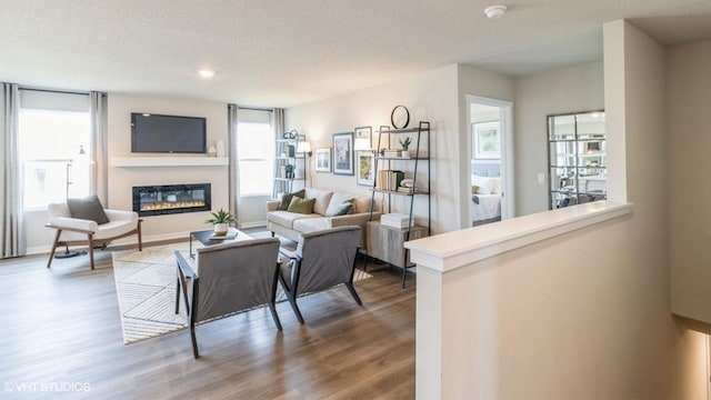 living area with a textured ceiling, wood finished floors, and a glass covered fireplace