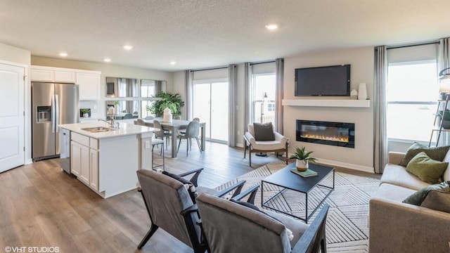 living room featuring a textured ceiling, recessed lighting, baseboards, light wood finished floors, and a glass covered fireplace