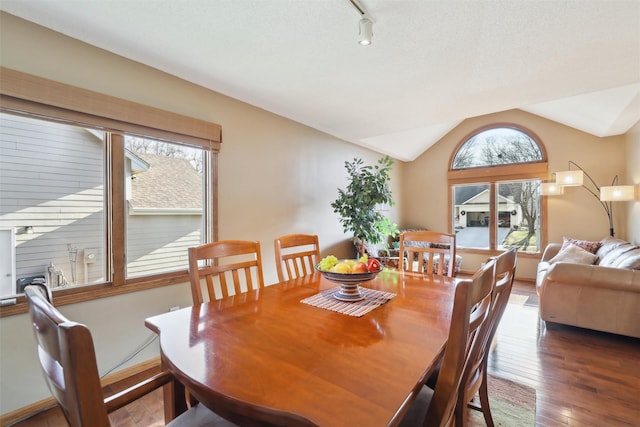 dining area with track lighting, hardwood / wood-style floors, baseboards, and vaulted ceiling