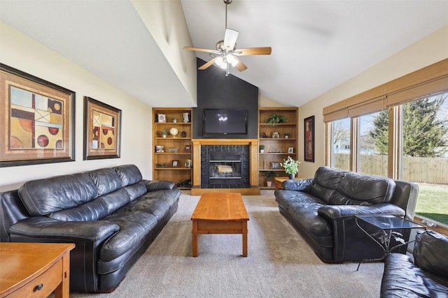 carpeted living room featuring a tile fireplace, built in shelves, vaulted ceiling, and ceiling fan