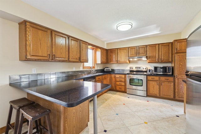 kitchen with kitchen peninsula, a textured ceiling, a kitchen bar, light tile patterned floors, and appliances with stainless steel finishes