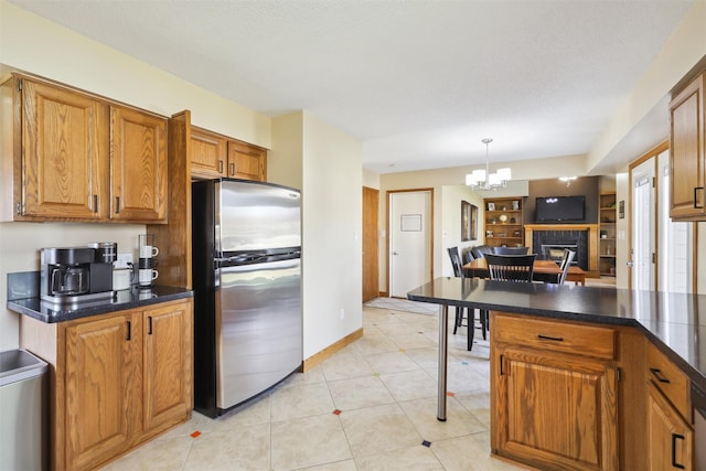 kitchen featuring dark countertops, light tile patterned flooring, brown cabinets, and freestanding refrigerator