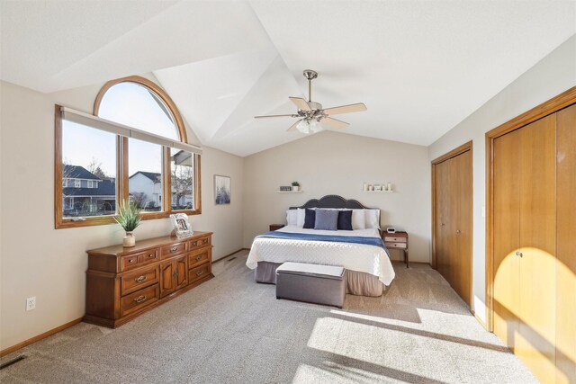 bedroom with two closets, baseboards, ceiling fan, light colored carpet, and vaulted ceiling