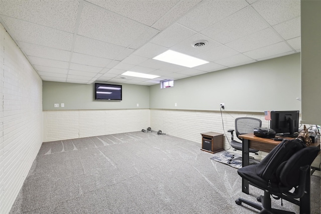 carpeted home office with a drop ceiling and brick wall