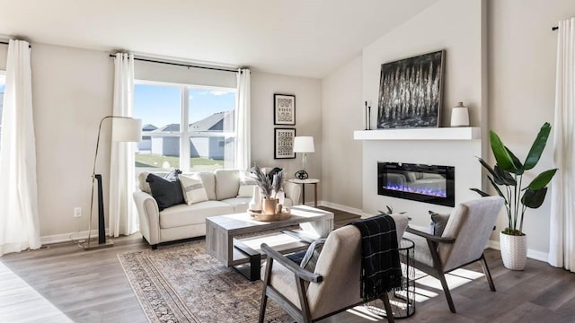 living area with a glass covered fireplace, baseboards, and wood finished floors