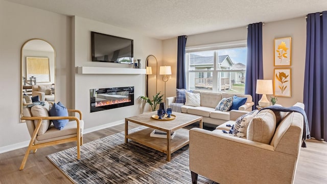 living area featuring arched walkways, a glass covered fireplace, a textured ceiling, wood finished floors, and baseboards