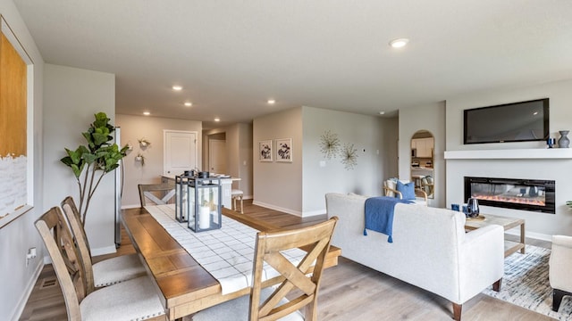 dining area with baseboards, light wood finished floors, a glass covered fireplace, and recessed lighting