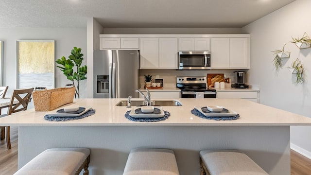 kitchen with light countertops, appliances with stainless steel finishes, light wood-style floors, white cabinets, and a sink