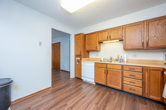 kitchen with wood finished floors, brown cabinetry, a sink, light countertops, and dishwasher