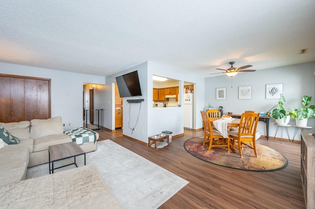 living area featuring wood finished floors, baseboards, a ceiling fan, visible vents, and a textured ceiling