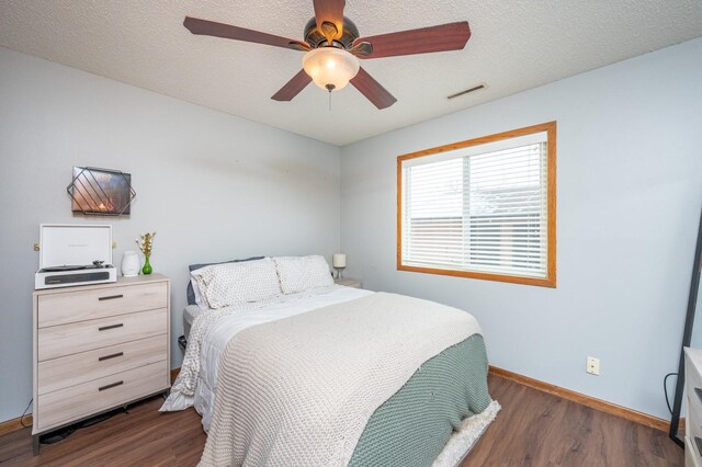 bedroom with baseboards, visible vents, dark wood-style flooring, ceiling fan, and a textured ceiling