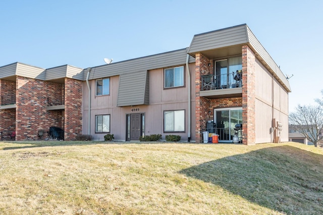 back of house with brick siding, a lawn, and a balcony