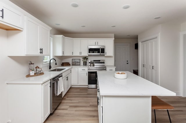 2503 Shaw St, Des Moines, IA 50317 - kitchen with appliances with stainless steel finishes, a sink, a kitchen island, light wood finished floors, and white cabinetry