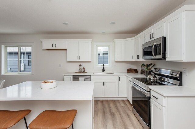 2503 Shaw St, Des Moines, IA 50317 - kitchen featuring appliances with stainless steel finishes, a sink, a kitchen breakfast bar, white cabinetry, and light wood finished floors