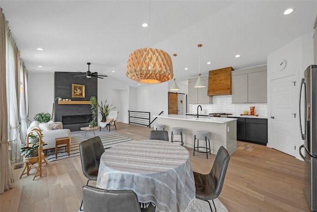 dining space with a fireplace, light hardwood / wood-style floors, ceiling fan, and lofted ceiling