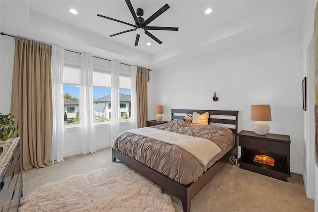 bedroom with a raised ceiling, ceiling fan, and light carpet