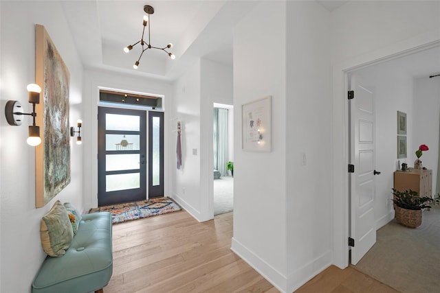 foyer entrance featuring light wood-type flooring, a raised ceiling, and a notable chandelier