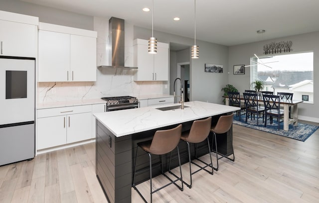 kitchen with white cabinets, sink, gas range, wall chimney exhaust hood, and an island with sink