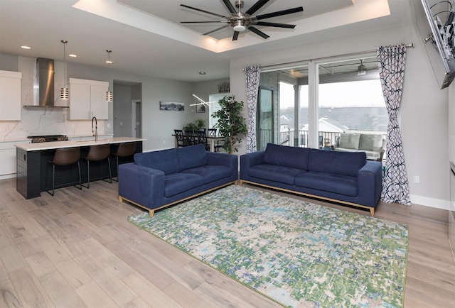 living room featuring ceiling fan, a raised ceiling, sink, and light hardwood / wood-style flooring