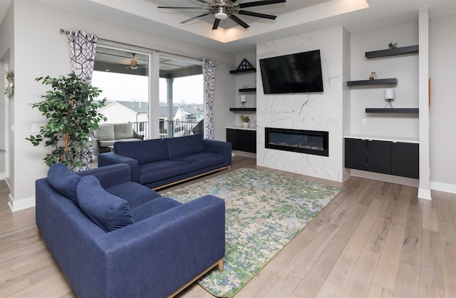 living room featuring ceiling fan, a raised ceiling, light wood-type flooring, and a high end fireplace