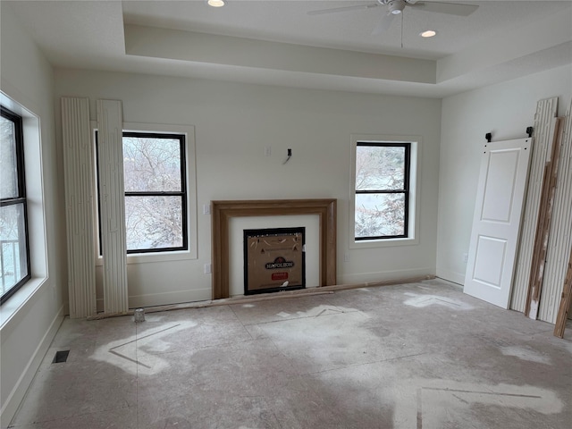 unfurnished living room featuring a barn door, a tray ceiling, and a wealth of natural light