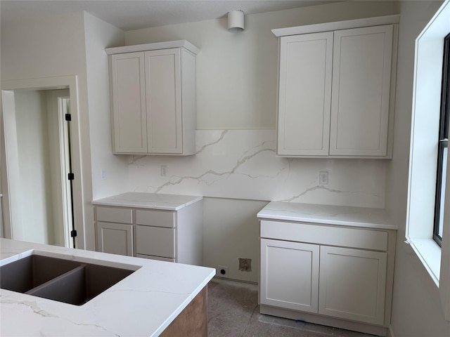 kitchen with white cabinetry, light stone counters, sink, and decorative backsplash