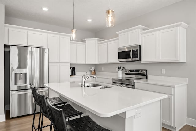 kitchen with appliances with stainless steel finishes, sink, pendant lighting, a center island with sink, and white cabinetry