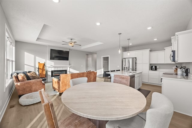 dining area with ceiling fan, light hardwood / wood-style floors, a raised ceiling, and a tile fireplace